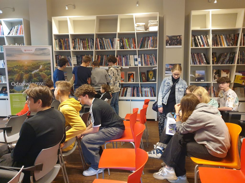 Uczniowie przeglądają komiksy dostępne  w  bibliotece francuskiej Alliance Française inni siedzą na krzesełkach i odpoczywają.