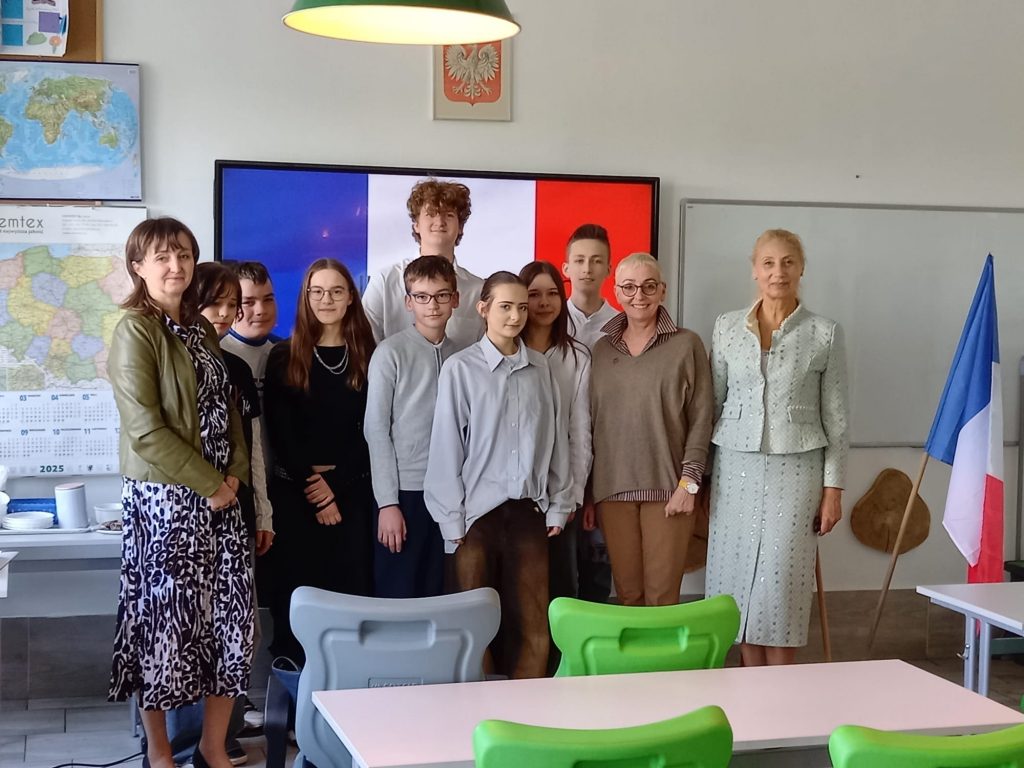 Laureaci konkursu wraz z nauczycielami stoją na tle flagi Francji wyświetlonej na tablicy w sali lekcyjnej