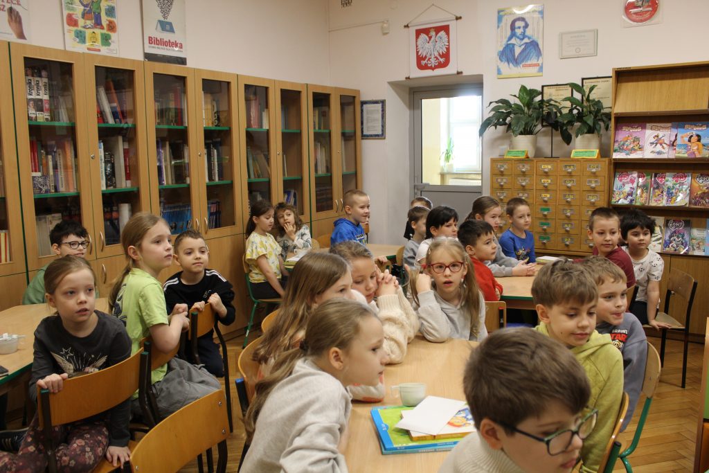 Uczniowie klas pierwszych siedzą przy stolikach i oglądają przedstawienie