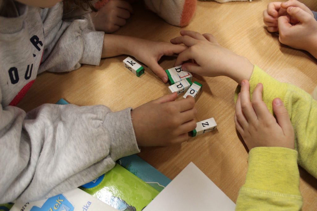 Dzieci rozwiązują zadanie. Widok blatu i elementów gry z literkami.