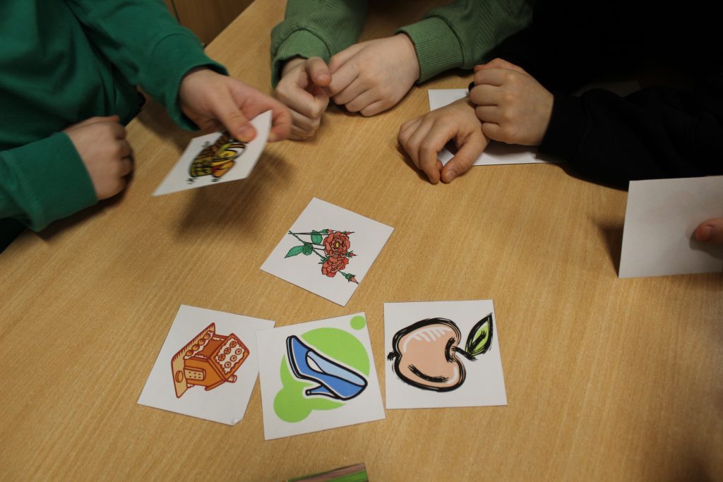 Dzieci rozwiązują zadanie. Widok blatu i elementów gry z obrazkami.